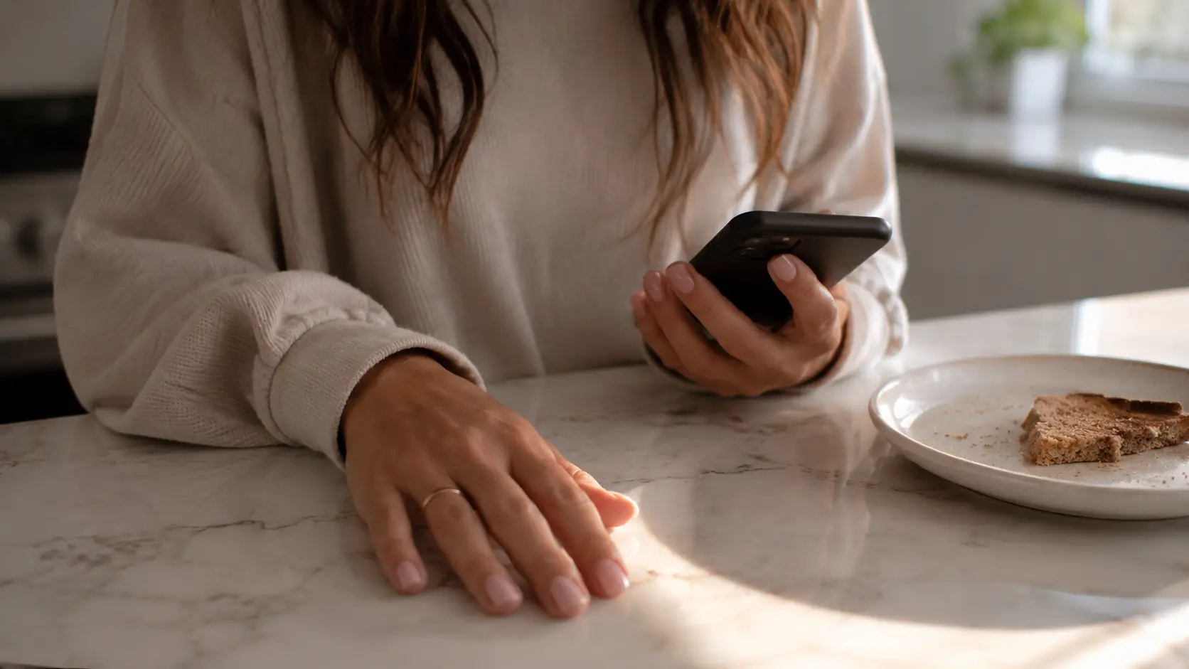 Astrology relationship needs — close-up of a woman's hands on a kitchen counter, phone face-down beside an untouched breakfast