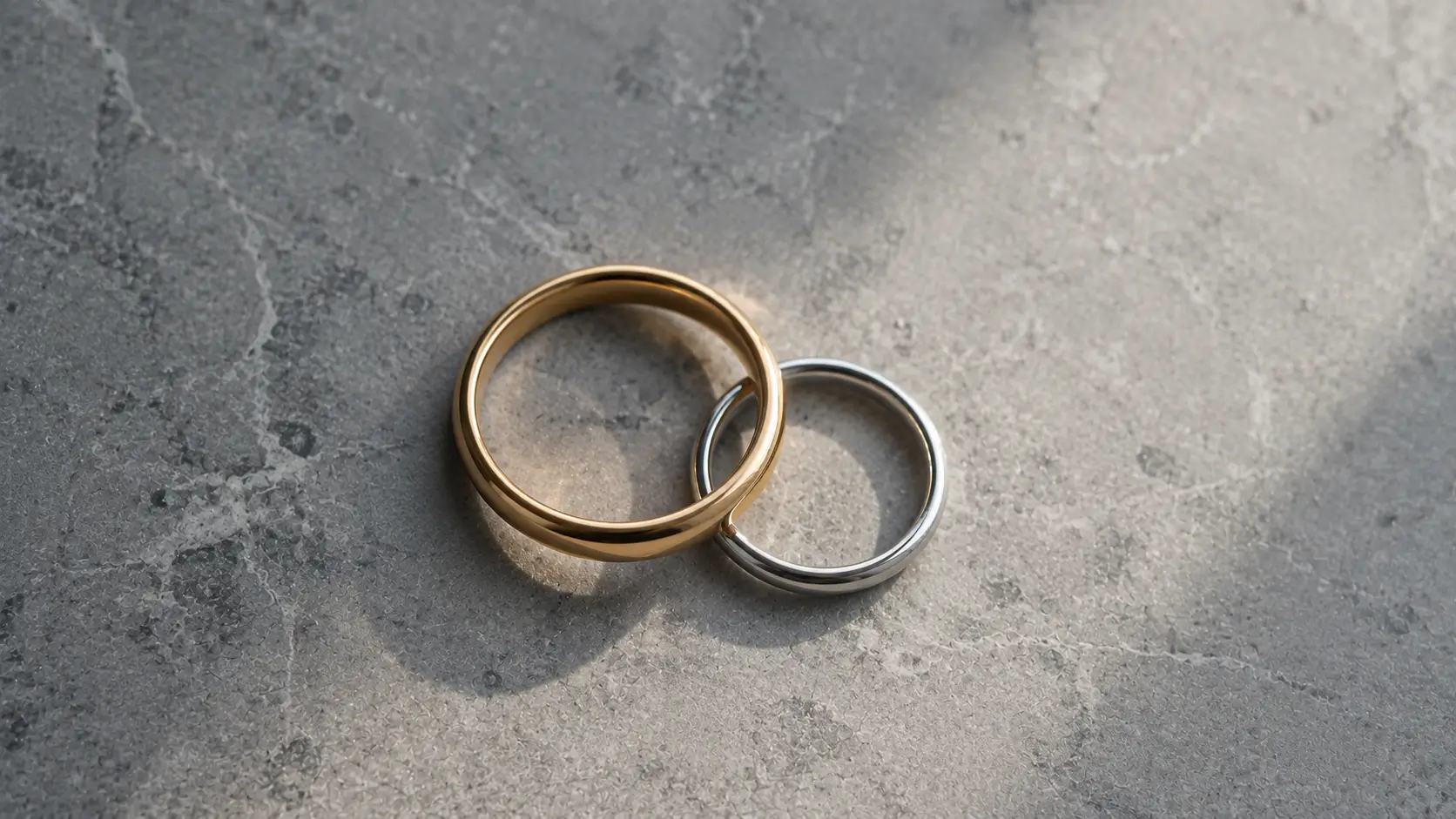 Birth chart relationship compatibility — two interlocking rings, one gold and one silver, on a matte stone surface in morning light