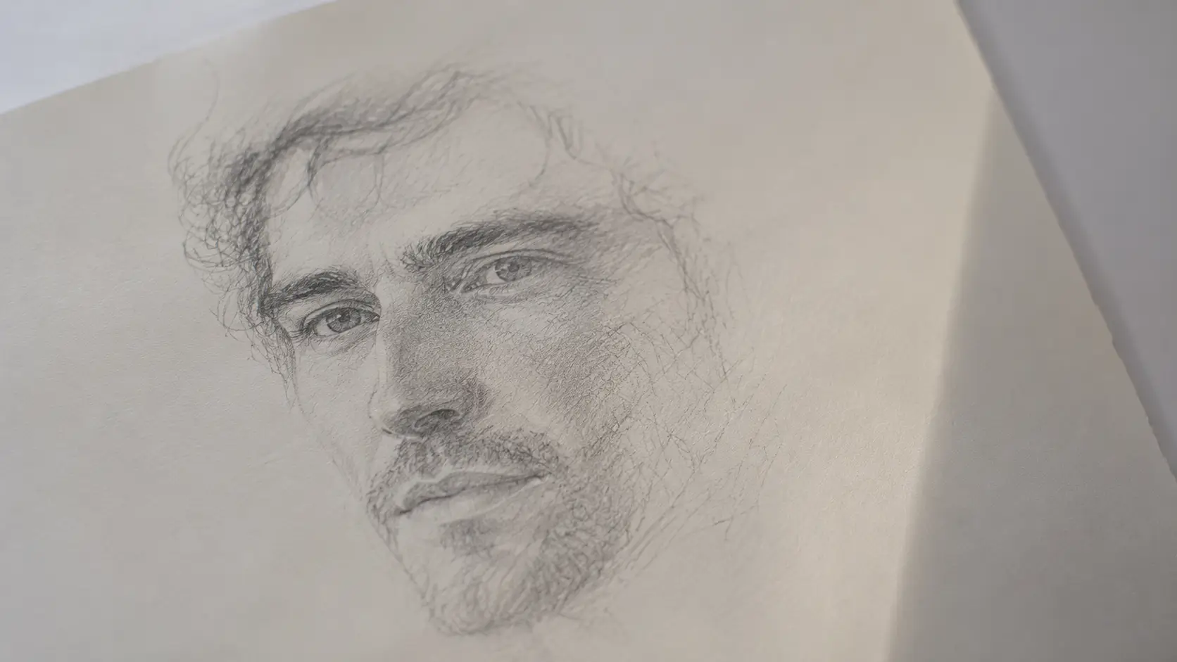 Birth chart soulmate reading — a pencil sketch portrait of a man's face, partially rendered, emerging from a white page in soft natural light, like a memory becoming real