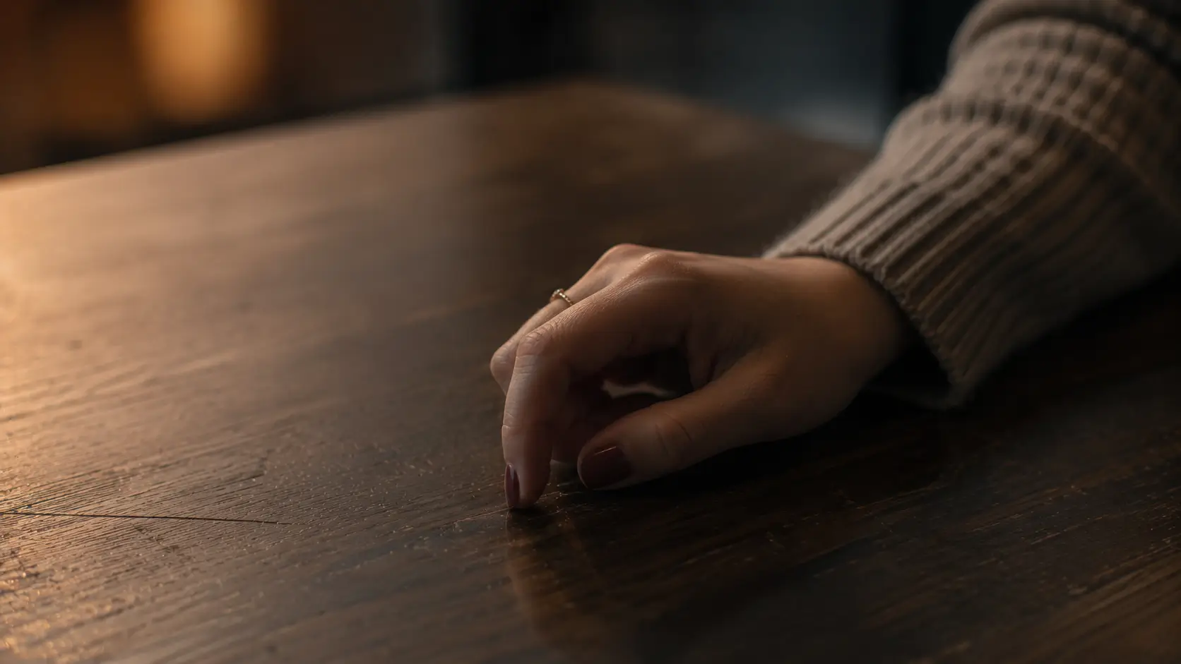 Emotionally unavailable men astrology — close-up of a woman's hand alone on a café table, fingers slightly curled, a ring visible