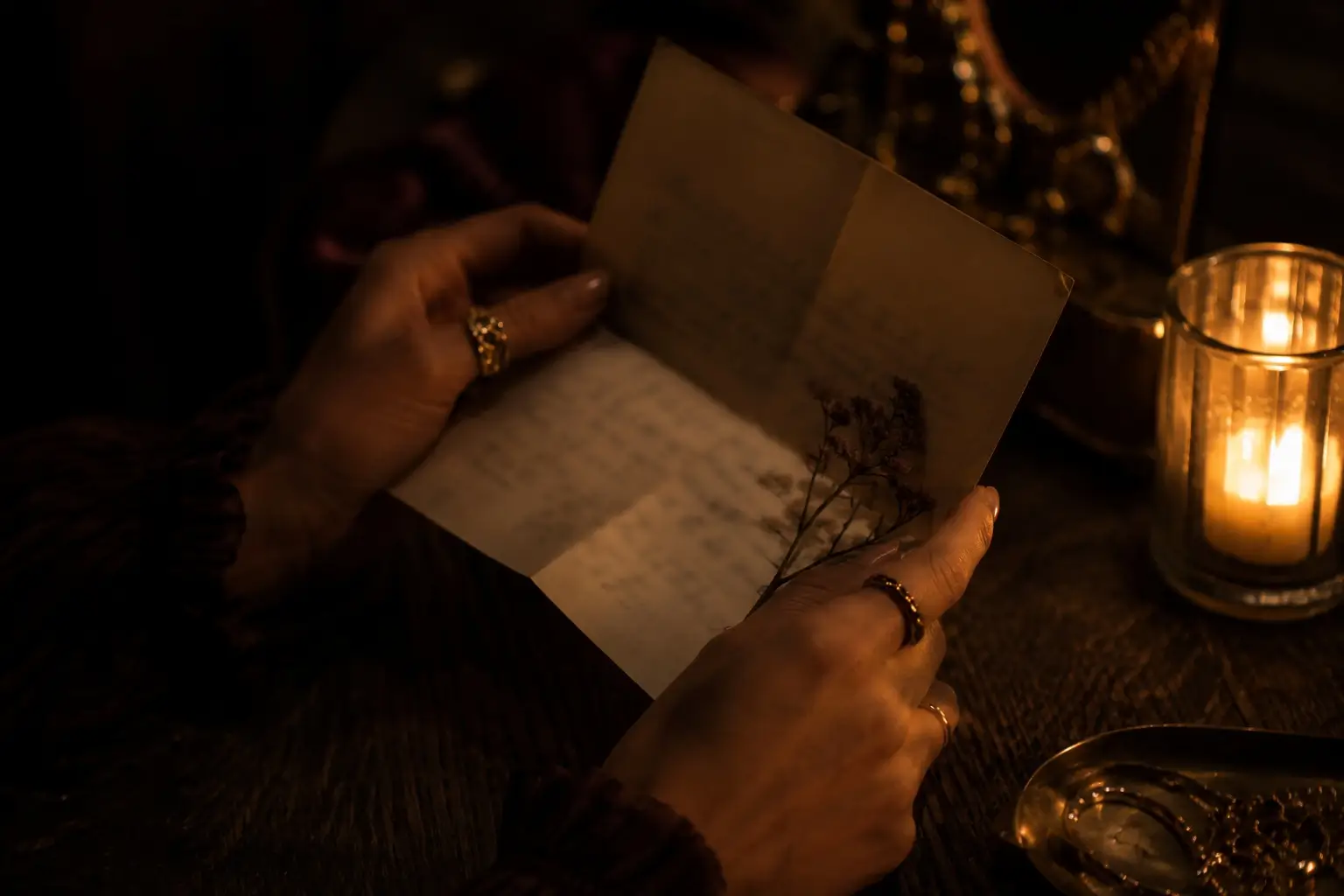gemini pisces love match — close-up of feminine hands holding an open letter by candlelight, warm gold rings, quiet emotional intimacy
