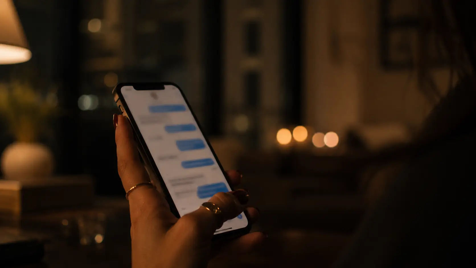 Gemini woman personality relationships — a woman's hand holding a phone scrolling through old texts at night, rings and faded nail polish, dim apartment light