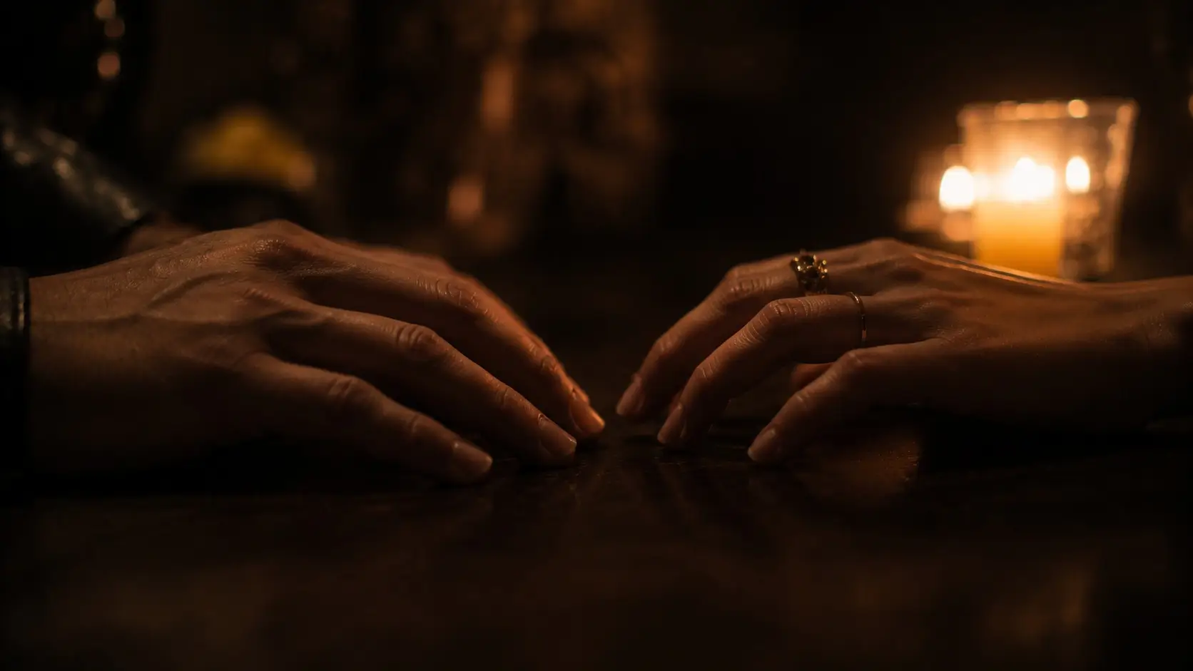 Leo scorpio attraction — two hands almost touching on a dark surface, candlelight, emotional tension