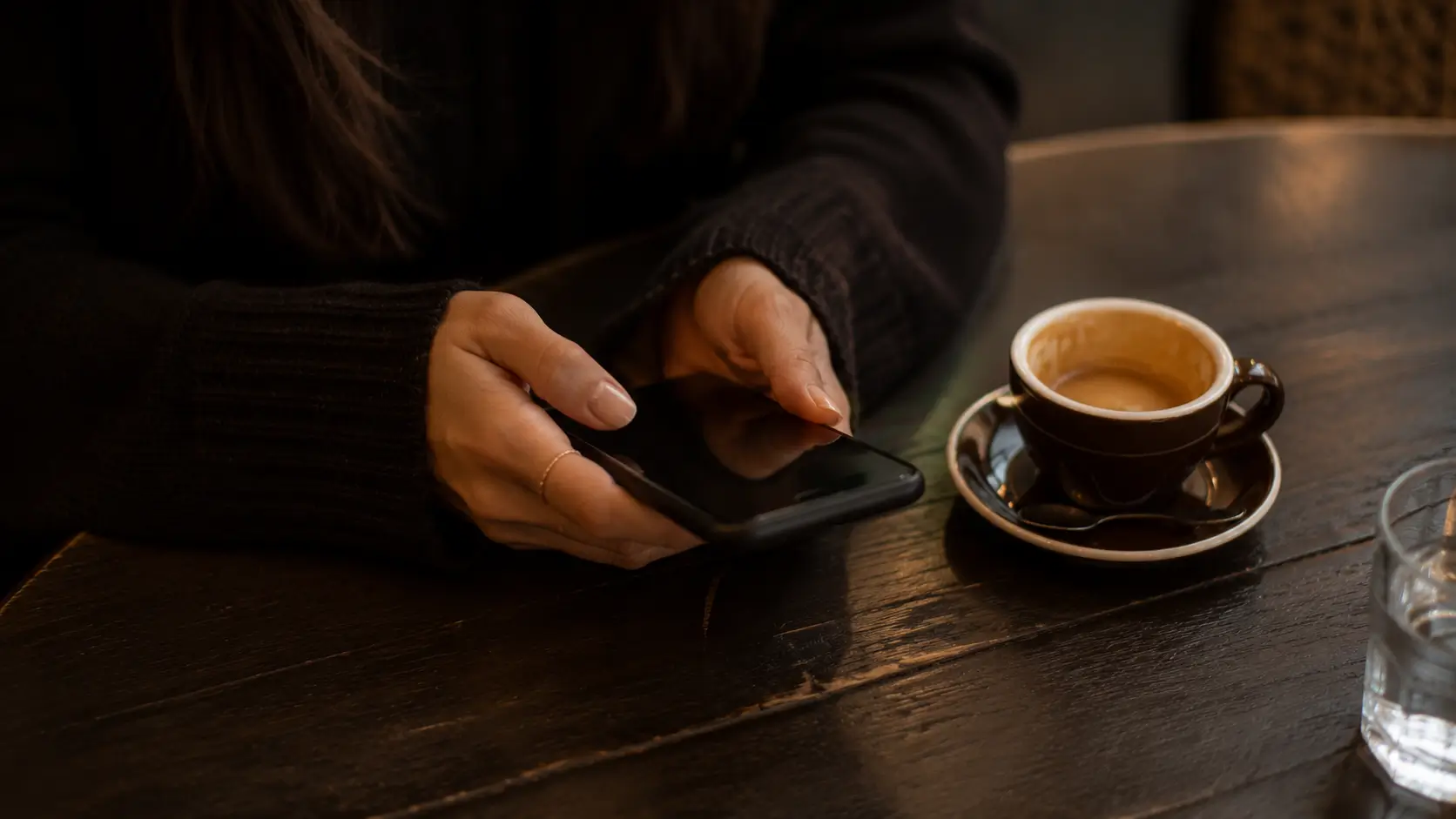 Scorpio woman love life problems — woman’s hands resting on café table beside a face-down phone, not checking it