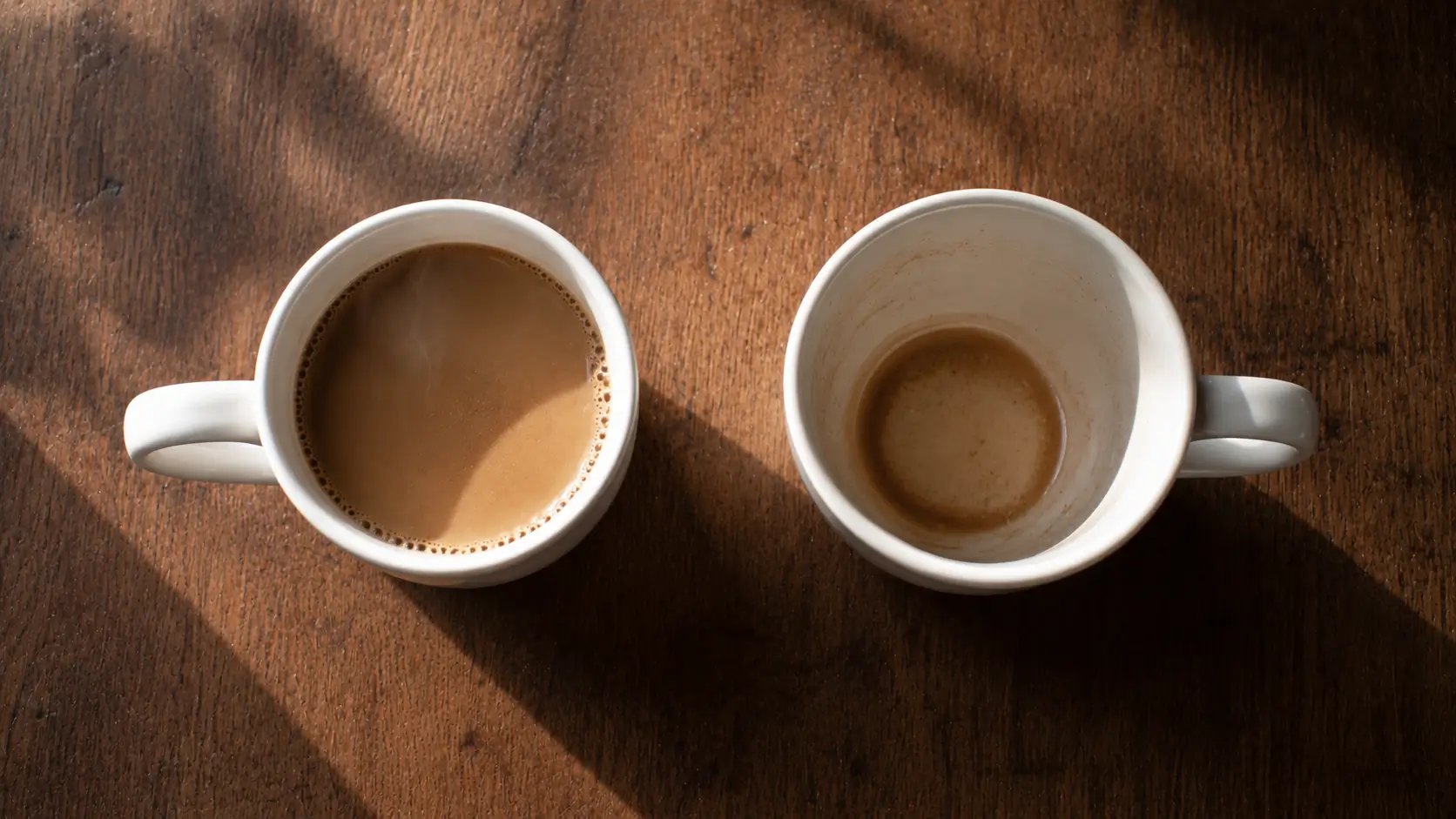 synastry compatibility long-term — two coffee cups side by side on a wooden table, one full and one nearly empty, morning light across the surface