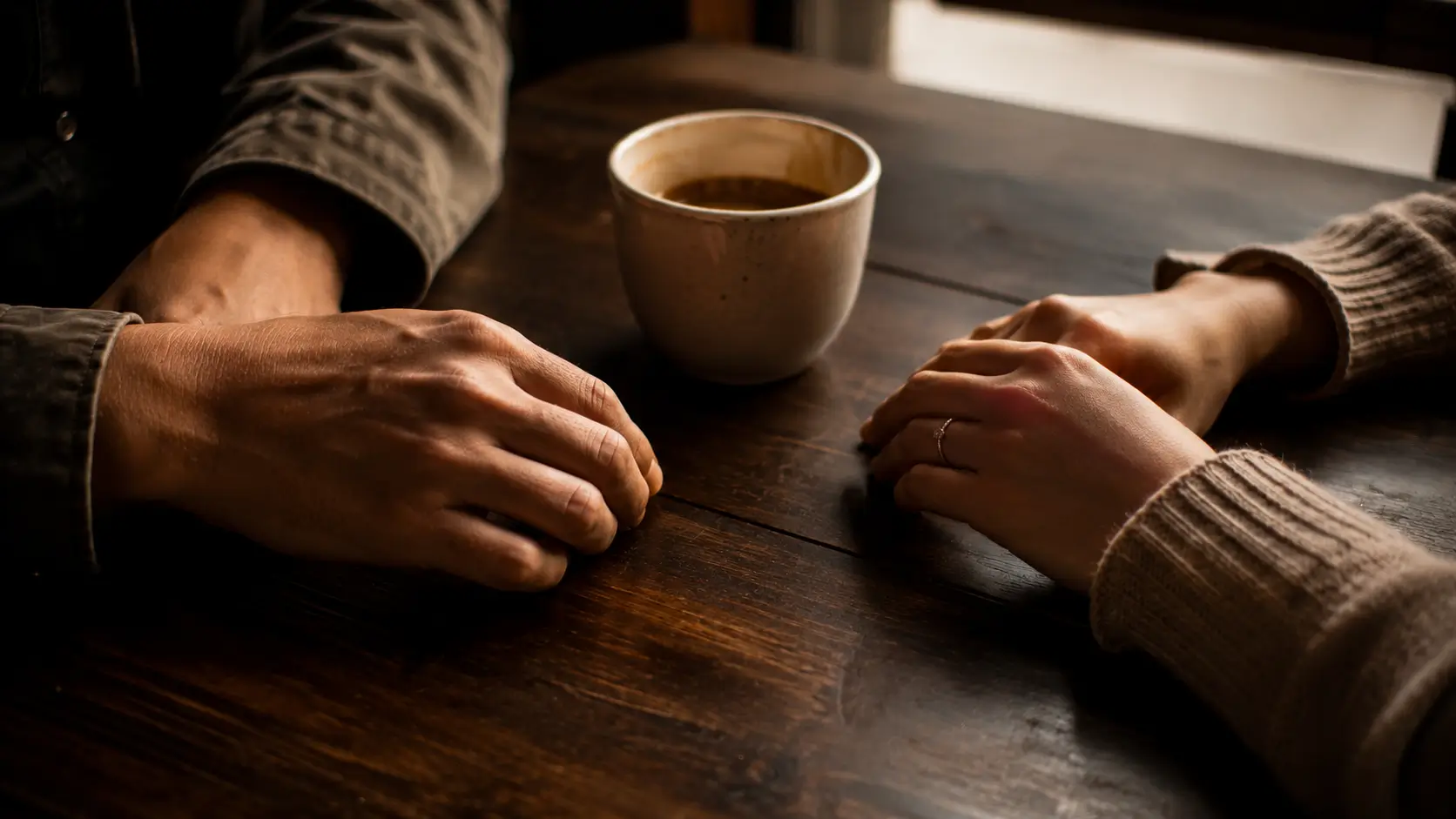 Taurus cancer relationship attraction — close-up of two pairs of hands near each other on a café table, not touching, soft warm light