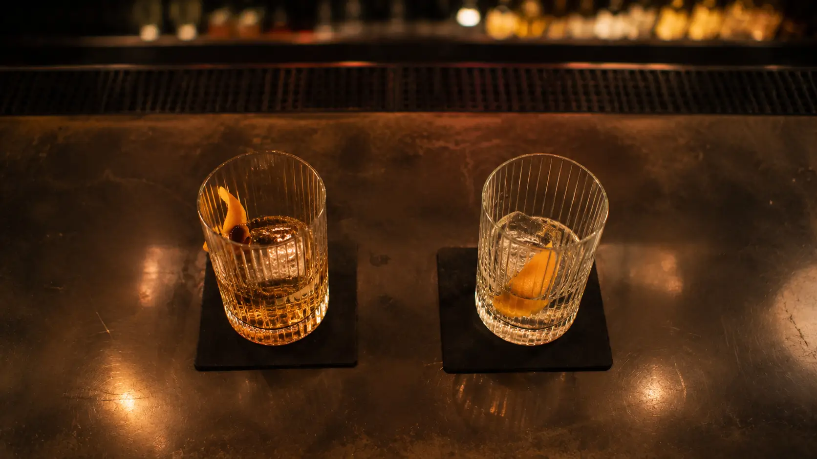 Why leo falls for scorpio — two drinks on a bar counter, one untouched, blurred crowd in the background, quiet tension