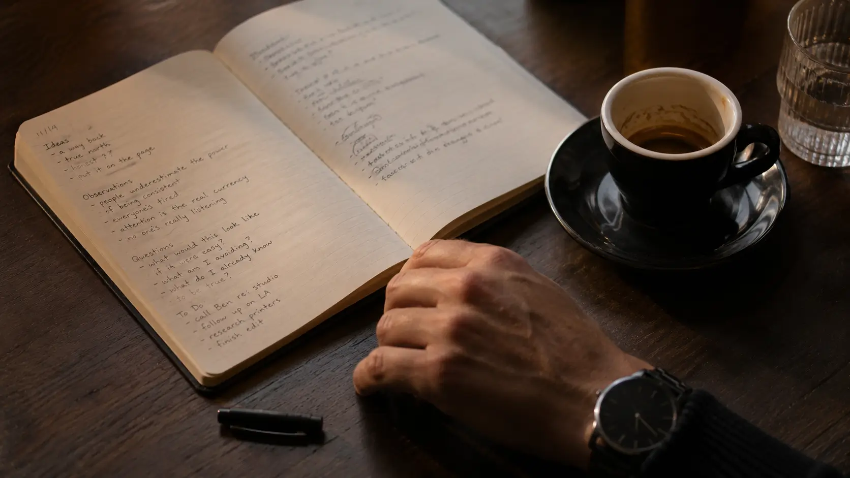 Why virgo man likes scorpio woman — close-up of a man's hand beside an open notebook and forgotten espresso, pen mid-thought