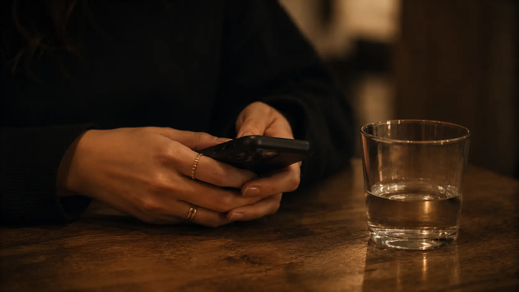 Zodiac signs when hurt in a relationship — close-up of a woman's hands holding a smartphone face-down on a wooden café table, not checking it
